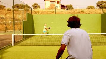 Una cancha de tenis con una red, un jugador con camisa blanca y otro con camisa amarilla.