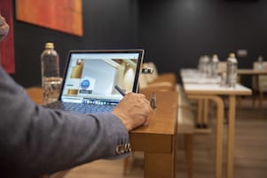 Una persona usando una computadora portátil en una mesa de madera en una habitación con una pared oscura y varias botellas de agua sobre la mesa.