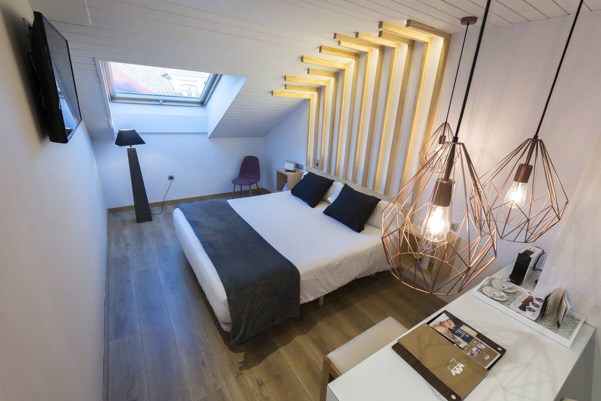 A modern bedroom with a skylight, a bed with a headboard, bedside tables, a desk, and a chair.