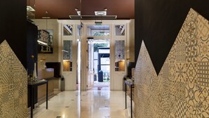 A hallway with patterned walls, a polished floor, and a view into a room with a window. - Hotel Fruela (Oviedo)