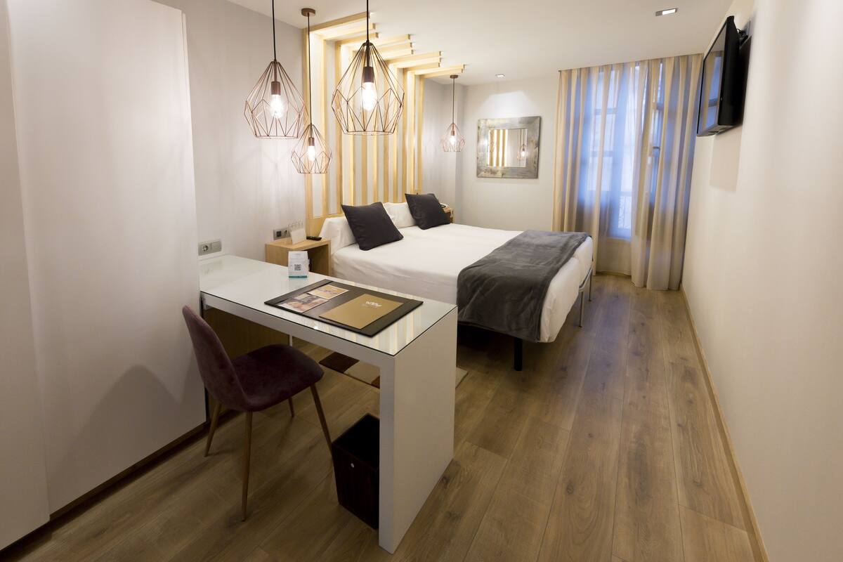 A compact hotel room with a bed, a desk with a chair, and a TV mounted on the wall.