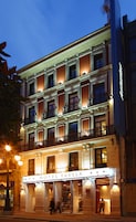 Un hotel de varios pisos con una fachada clásica, balcones y una entrada bien iluminada.