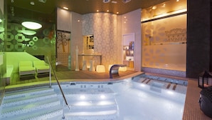 A modern spa with a large hot tub, a reception area, and a seating area with a green sofa. - Hotel Fruela (Oviedo)