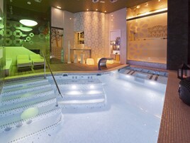 Un spa moderno con un jacuzzi grande, una zona de recepción y un área de descanso con un sofá verde.