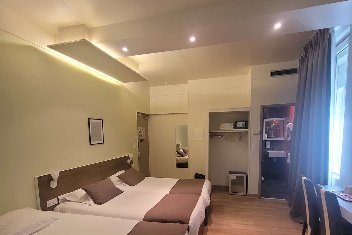 Una habitación de hotel con dos camas, un escritorio, una silla, un espejo y un armario.