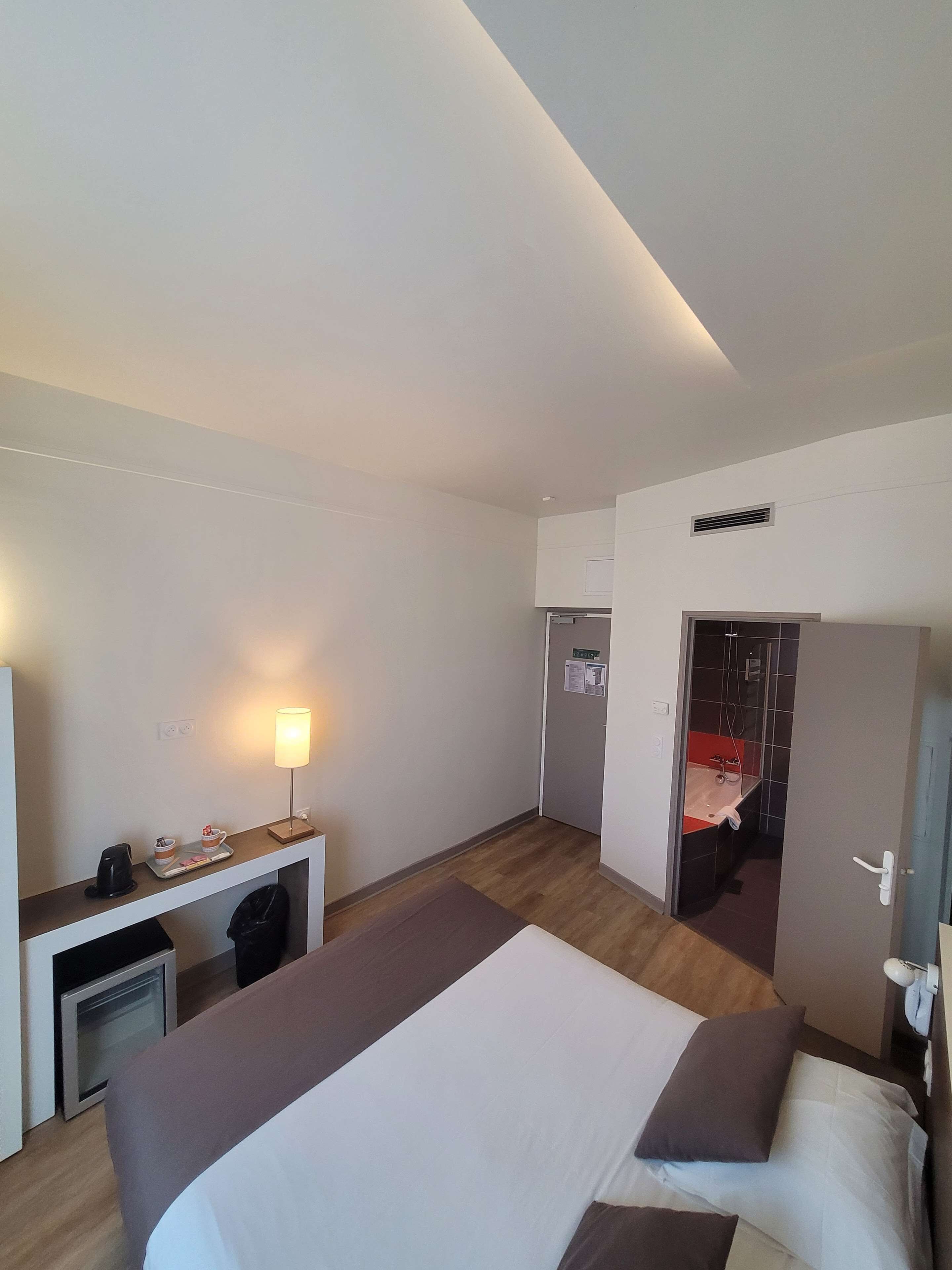 A hotel room with a bed, bedside table, lamp, and a view of the bathroom.