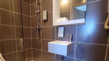Ein modernes Badezimmer mit einer gläsernen Dusche, einem weißen Waschbecken und einem Spiegel darüber.