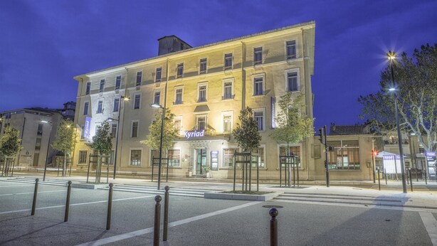 A multi-story hotel with a sign reading "Kyriad" at the entrance, featuring a classic architectural style with evenly spaced windows and a flat roof. - Kyriad Orange Centre (Orange)