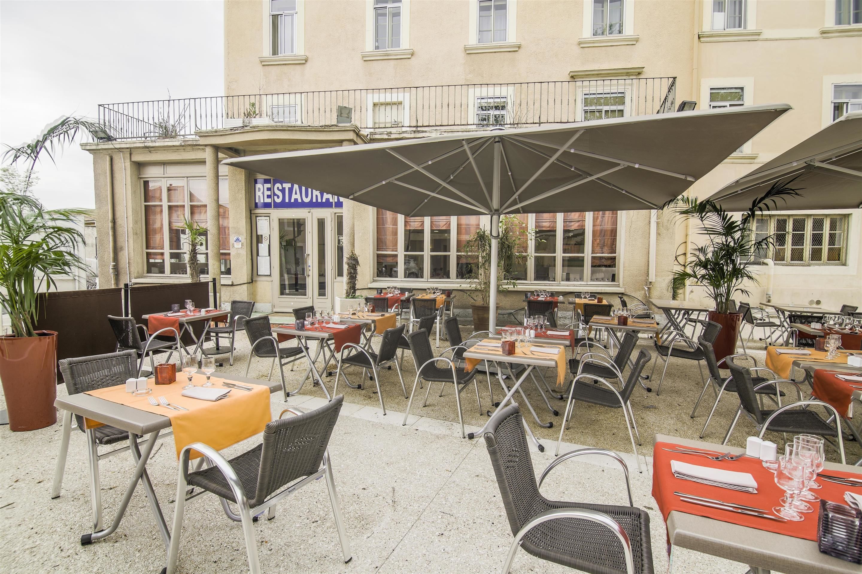 An outdoor cafe with tables and chairs, a sign for a restaurant, and a building in the background.