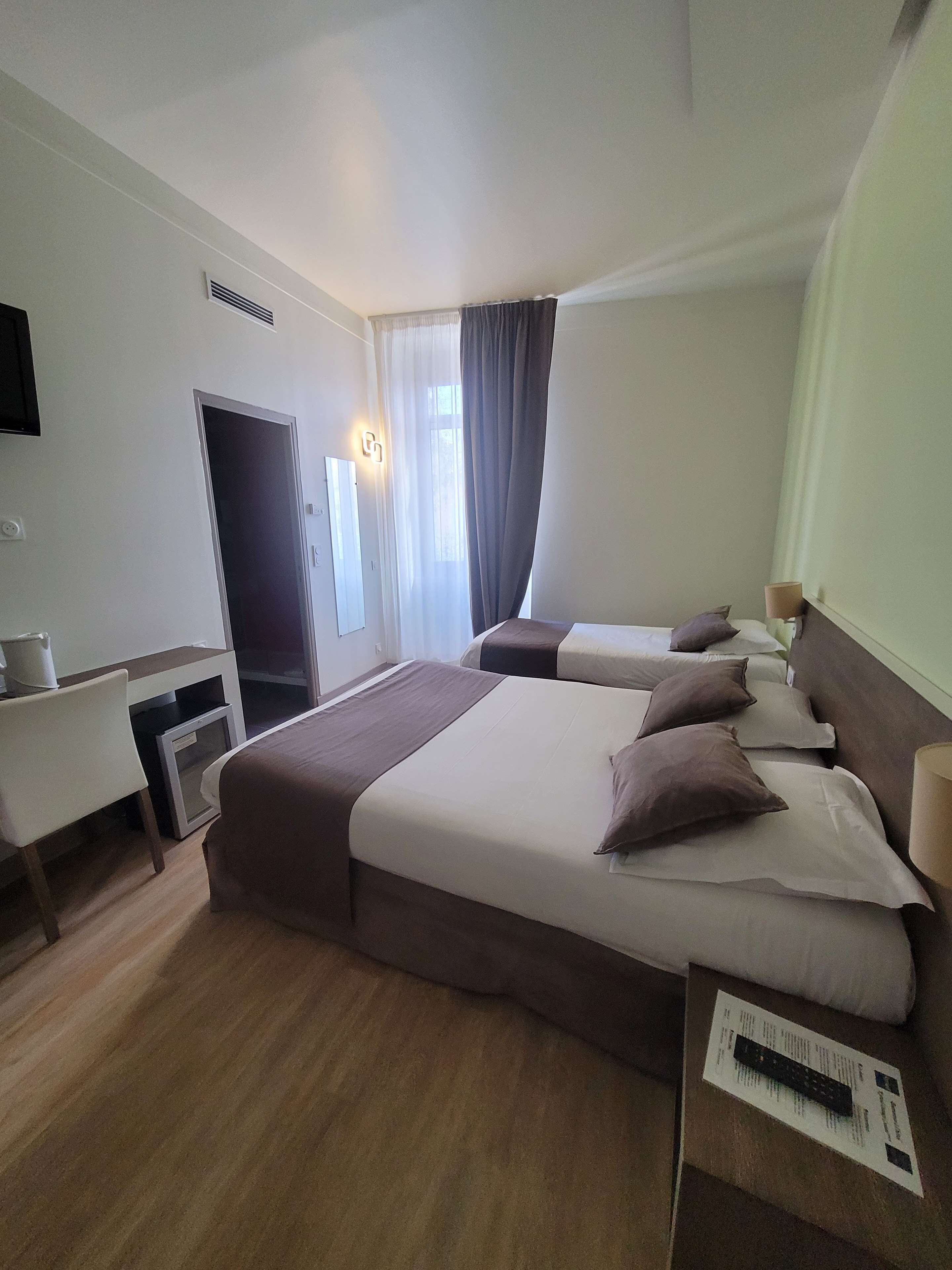 A hotel room with two beds, a desk, a television, and a window with curtains.