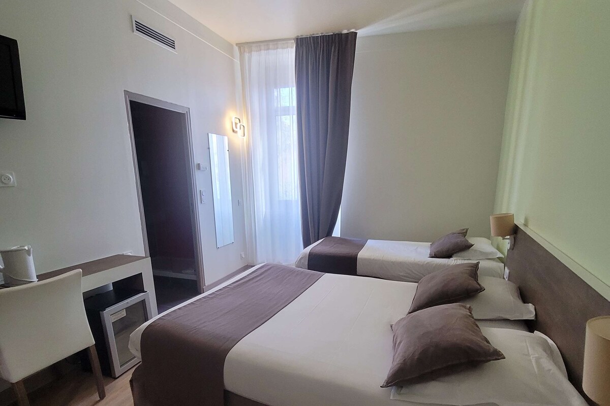 Habitación de hotel con dos camas, un escritorio, una televisión y una ventana con cortinas.