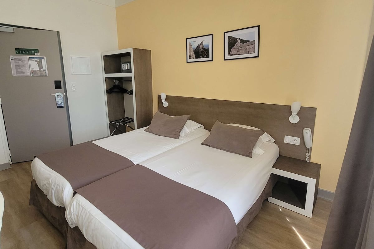 Una cama doble con cabecera marrón, una mesita de noche con un teléfono y una pequeña estantería.