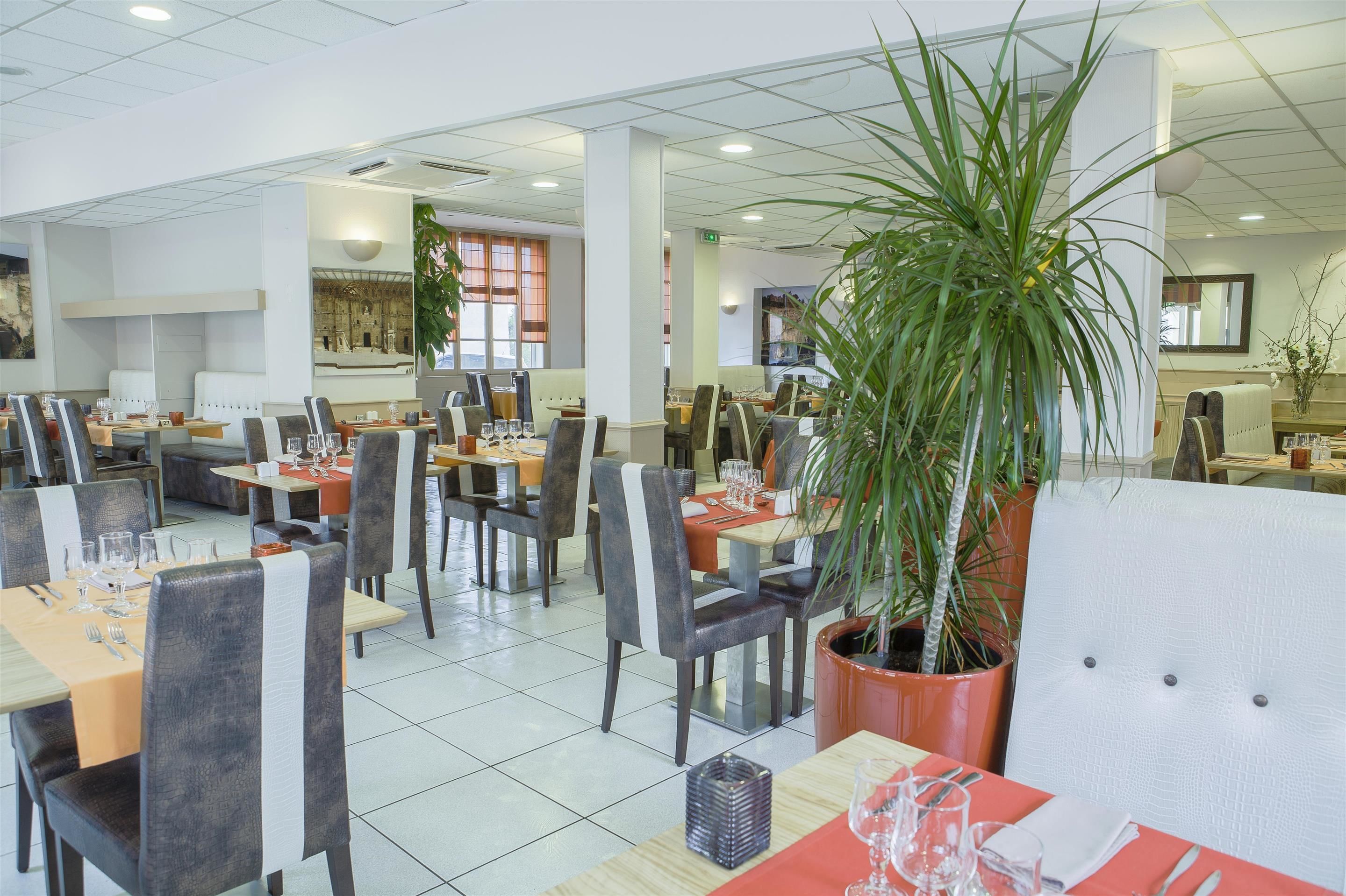 Un restaurante espacioso con numerosas mesas y sillas, grandes macetas con plantas y una decoración interior moderna y cuidada.