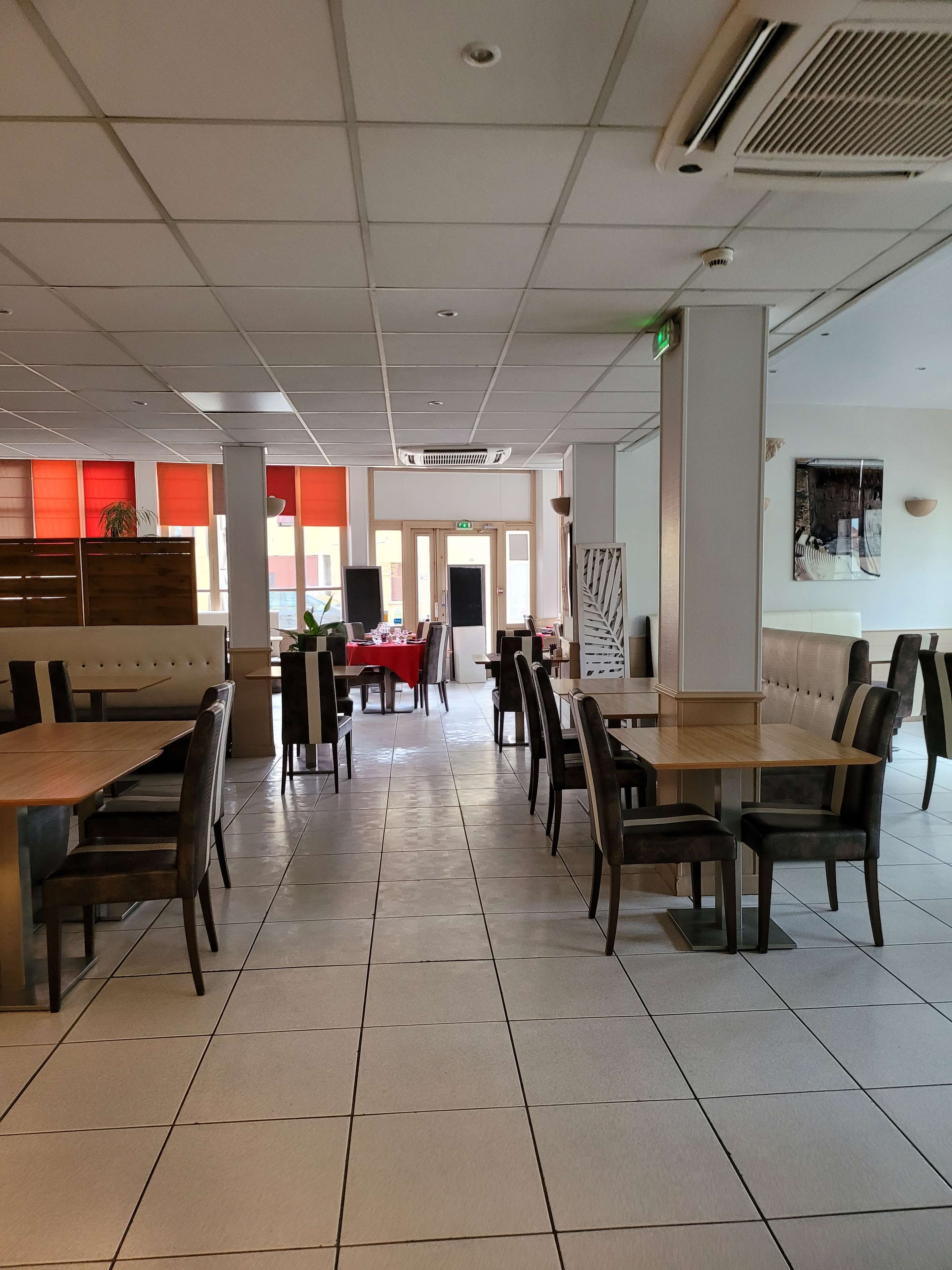 Un comedor amplio con mesas altas y sillas, una mesa central roja y vistas a la calle a través de grandes ventanales.