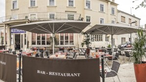 An outdoor bar-restaurant with tables and umbrellas, surrounded by potted plants and a building in the background. - Kyriad Orange Centre (Orange)