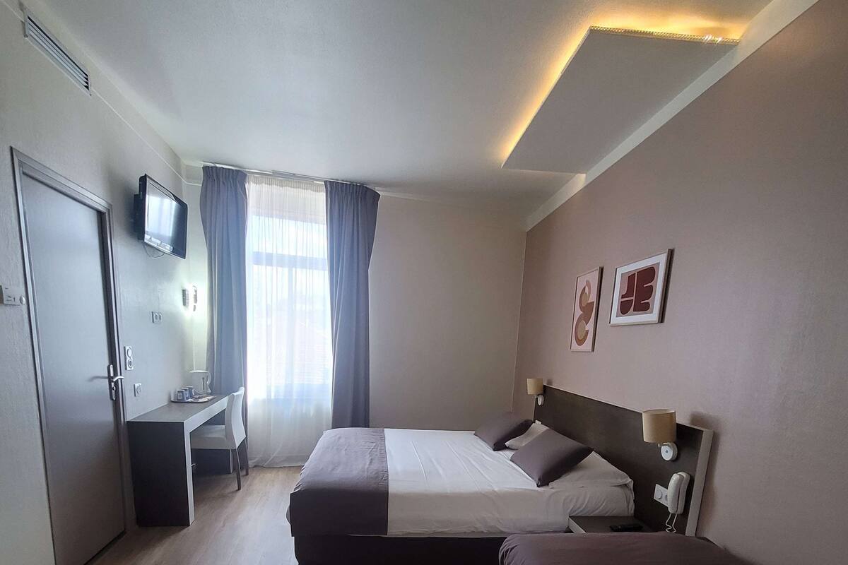 Habitación de hotel con dos camas, un escritorio, un televisor y una ventana con cortinas.