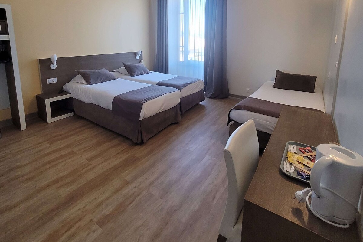 Habitación de hotel con dos camas, un escritorio y una silla, una mesita con una bandeja de aperitivos y una ventana con cortinas.