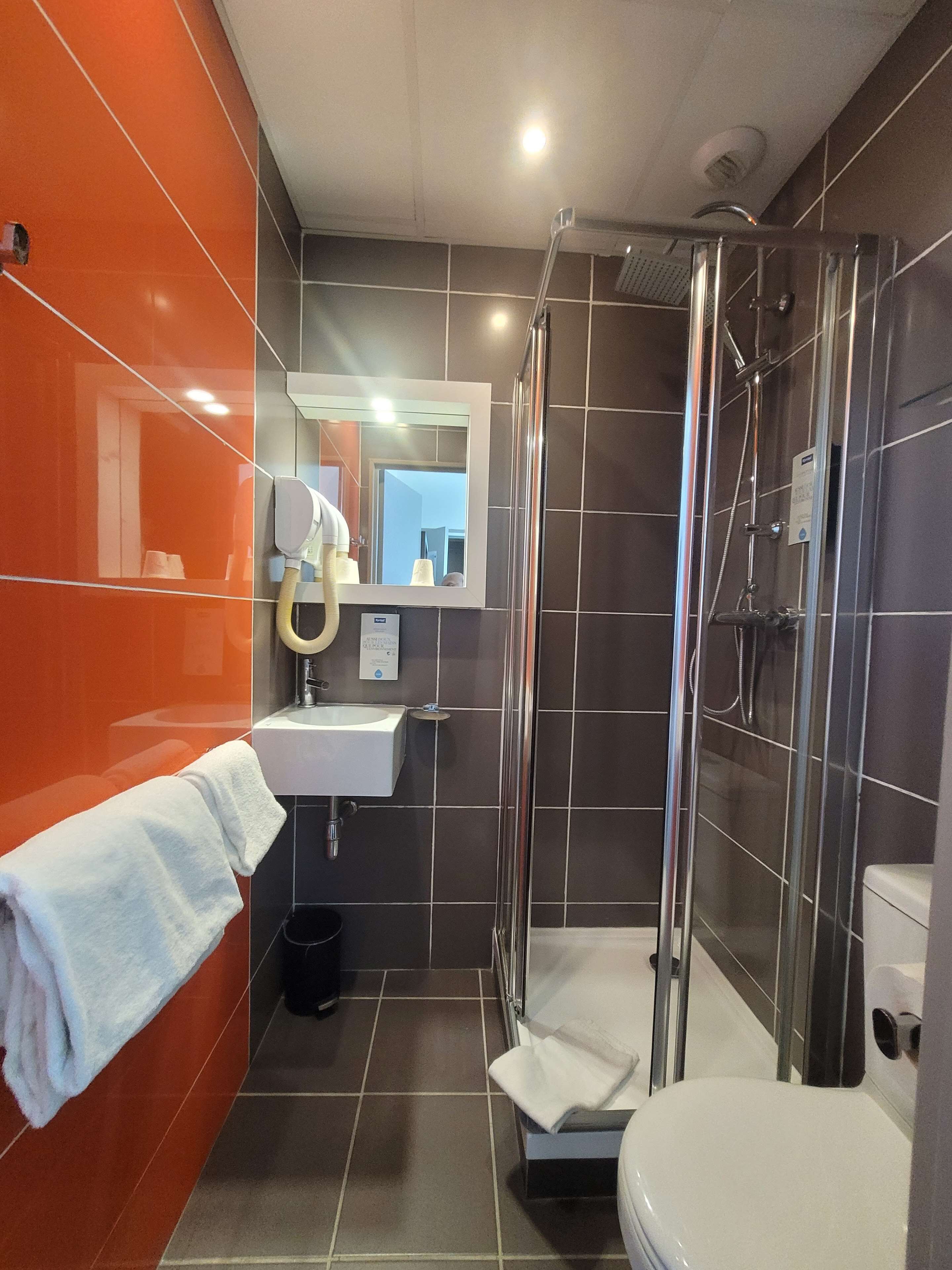 Et lille badeværelse med en brusekabine i glas, en hvid vask og et toilet.