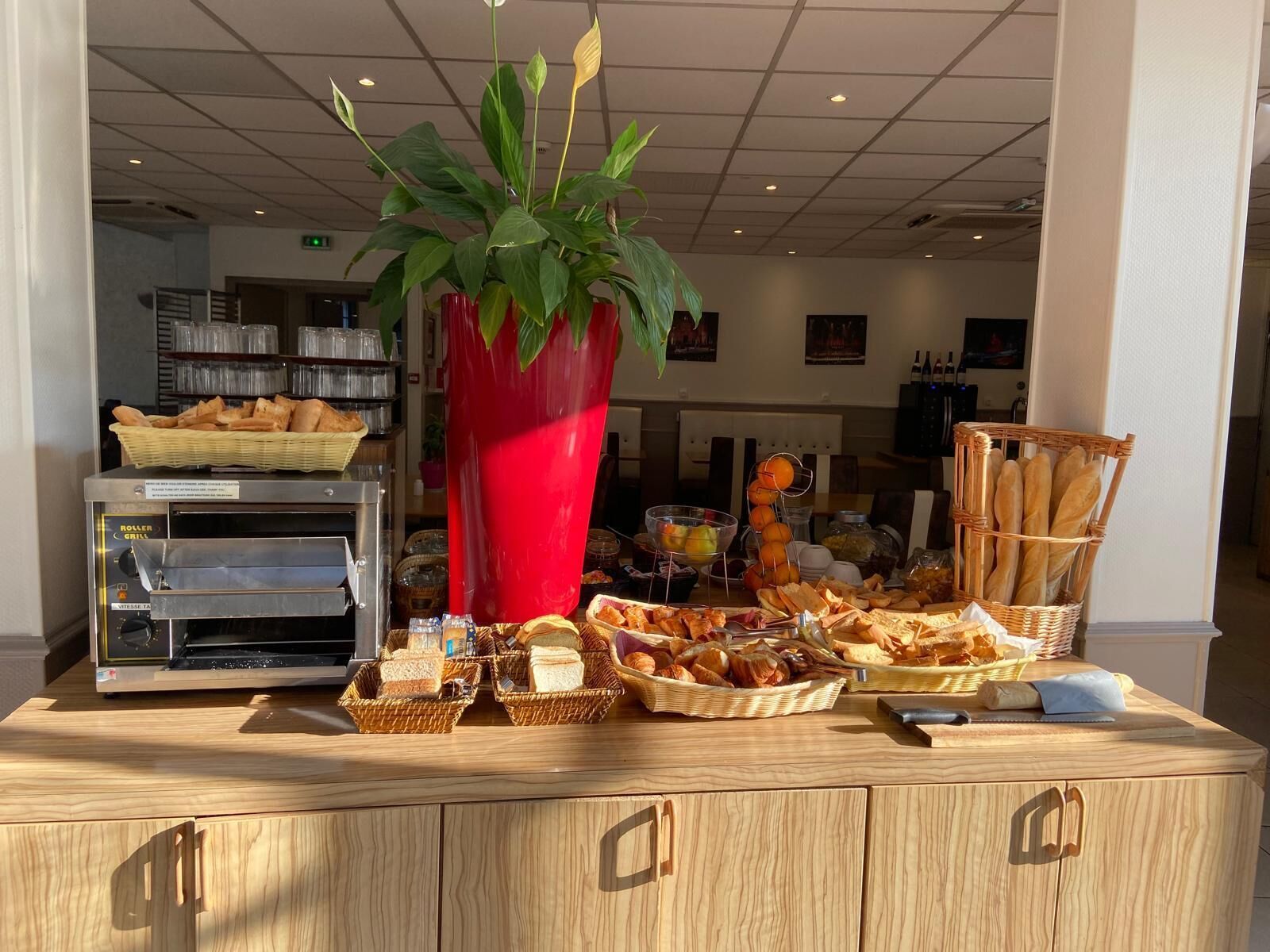 A buffet setup with various food items, a red vase with green leaves, and a bread display.