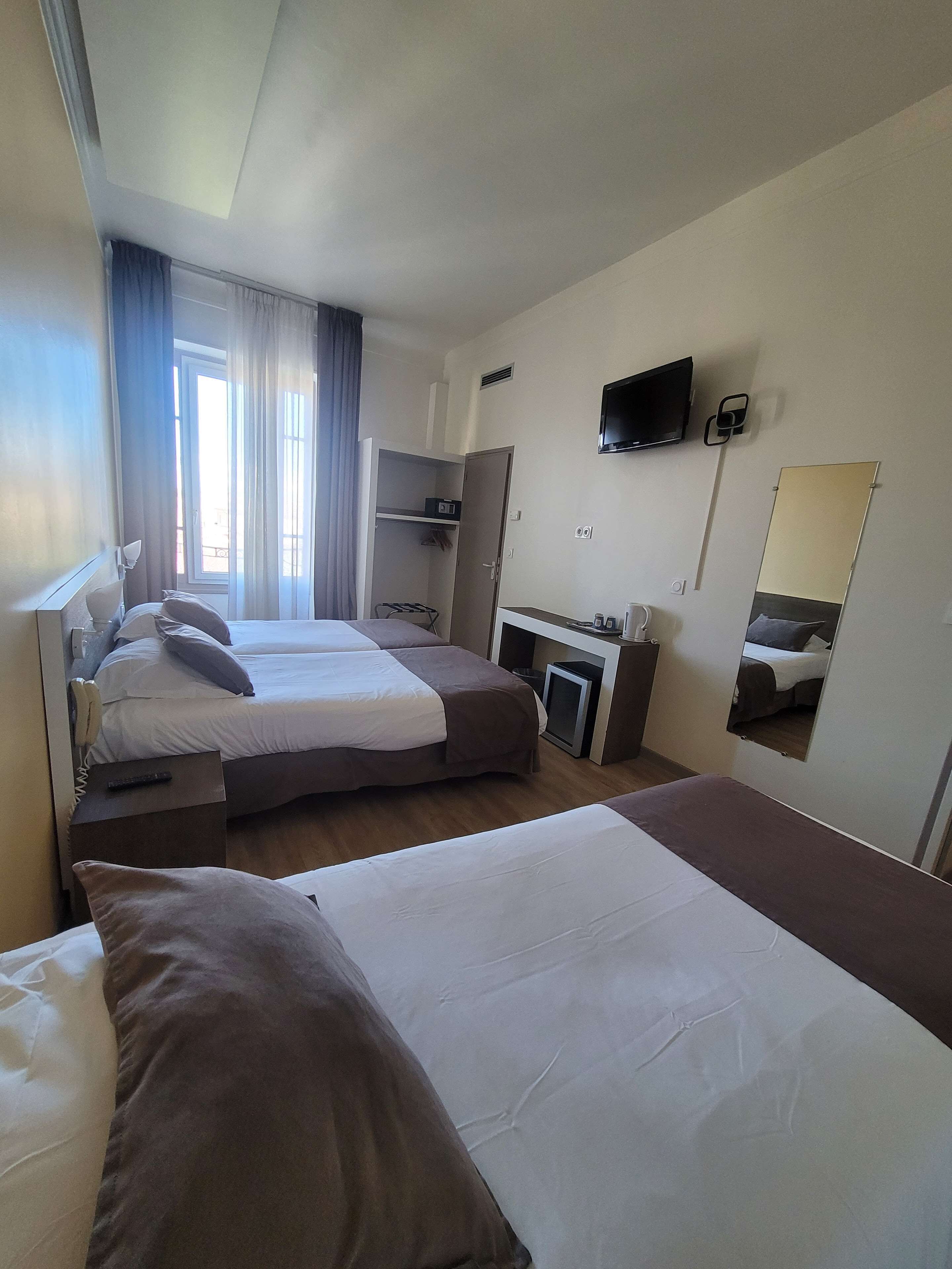 Habitación de hotel con dos camas, un escritorio con silla, televisor montado en la pared y ventana con cortinas.