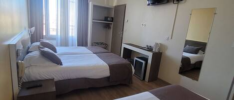Habitación de hotel con dos camas, un escritorio con silla, televisor montado en la pared y ventana con cortinas.