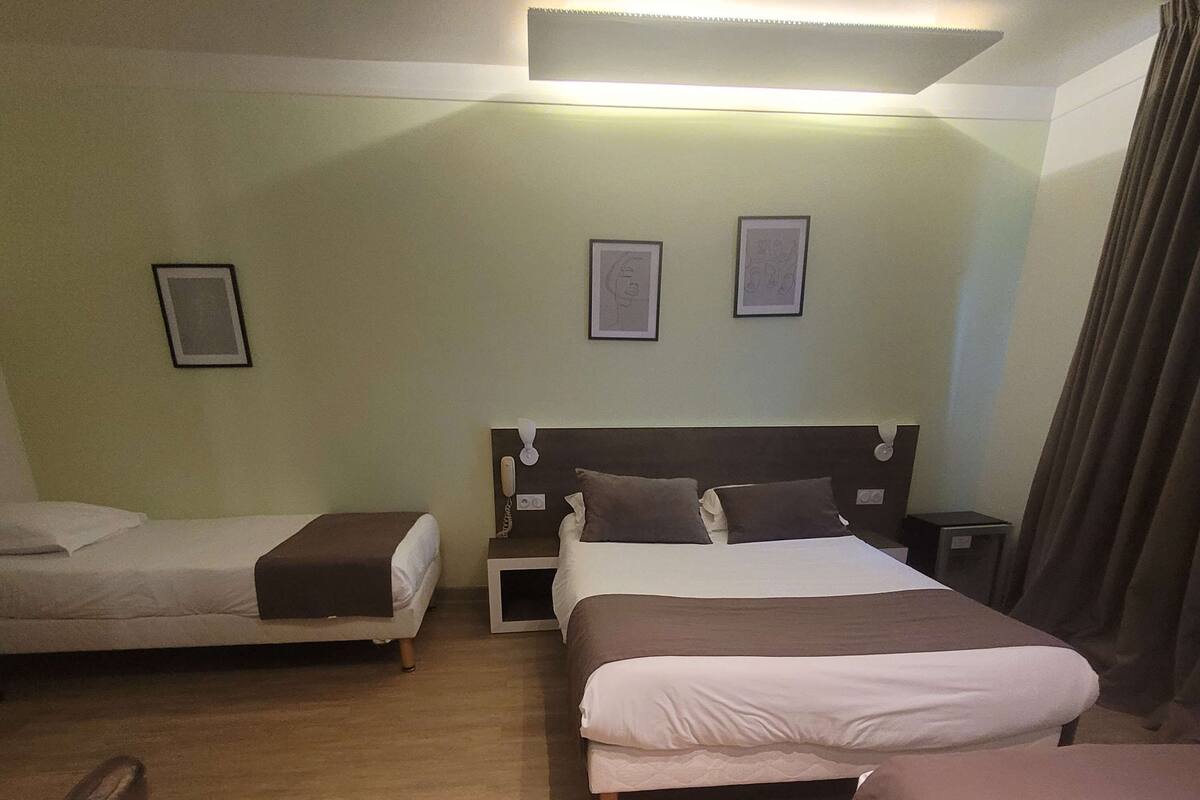 Habitación de hotel con dos camas individuales, una cama doble, una mesita de noche con lámpara y un teléfono instalado en la pared.
