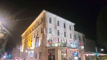A multi-story hotel with a restaurant on the ground floor, flags on the balcony, and a pedestrian crossing in front.
