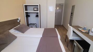 A hotel room with two beds, a desk, a mirror, a wardrobe, and a small kitchenette.