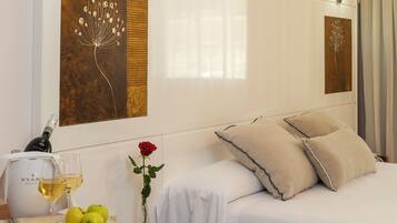 A hotel room with a bed, bedside lamps, a table with a bottle of wine, glasses, and apples.