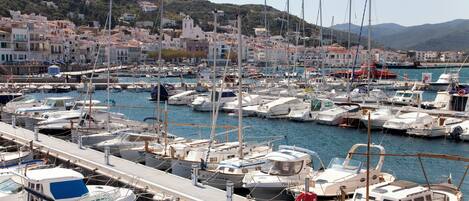 A marina with numerous boats docked, a pier extending into the water, and a backdrop of buildings and hills.