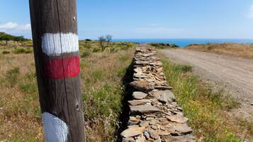 Ein Feldweg mit einer Steinmauer und einem Holzbalken mit weißen und roten Markierungen.