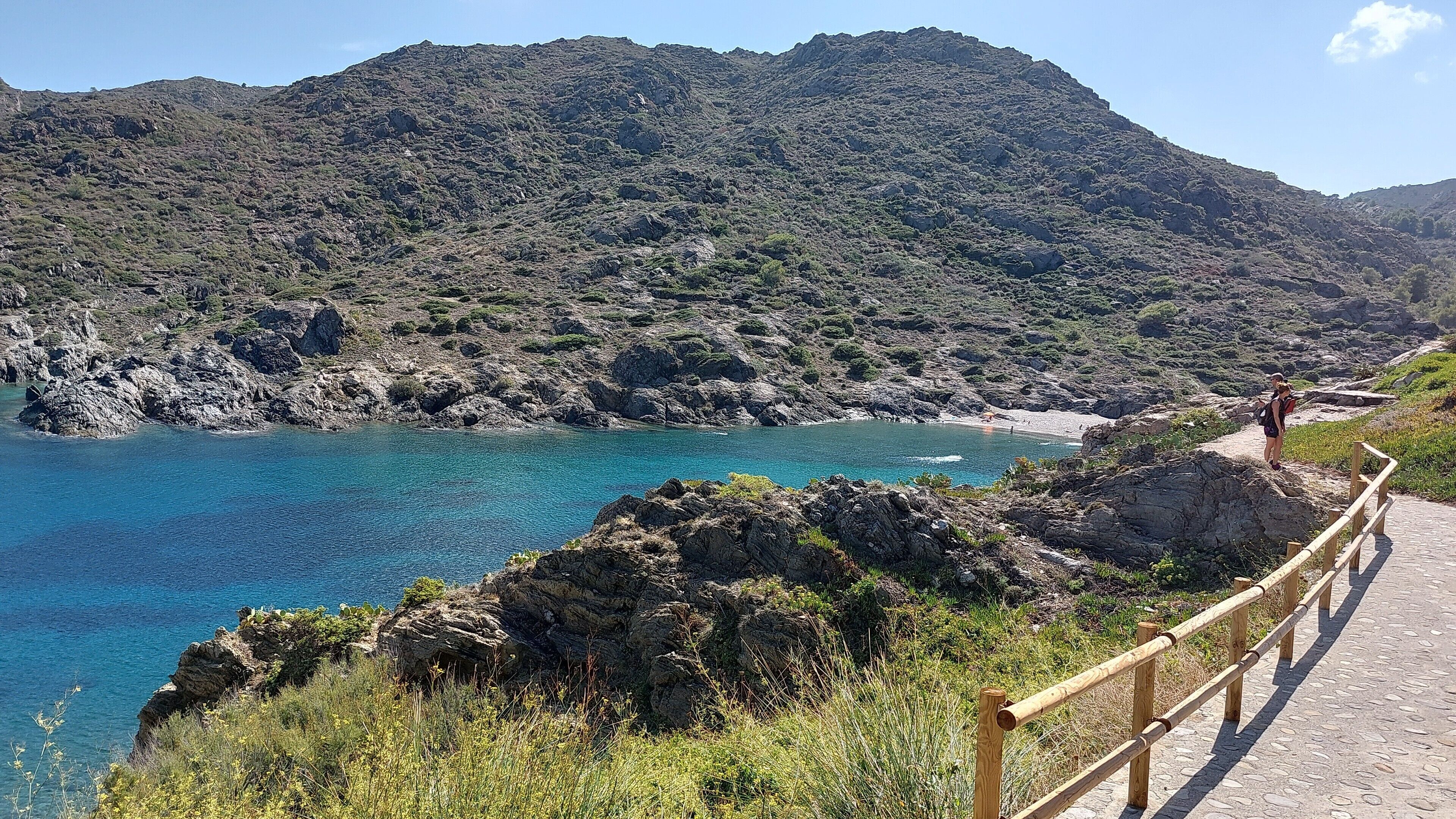 A coastal path with a wooden railing, rocky terrain, and a mountain in the background.