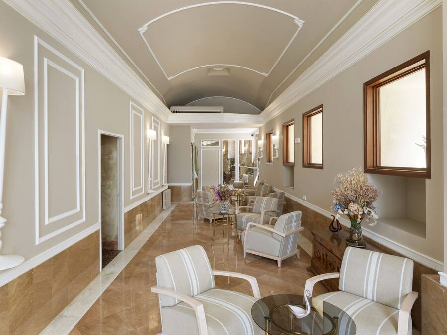 Un hall d’entrée spacieux, doté d’un sol en marbre, de portes à cadre blanc et d’un coin salon avec des chaises à rayures et une table en verre.