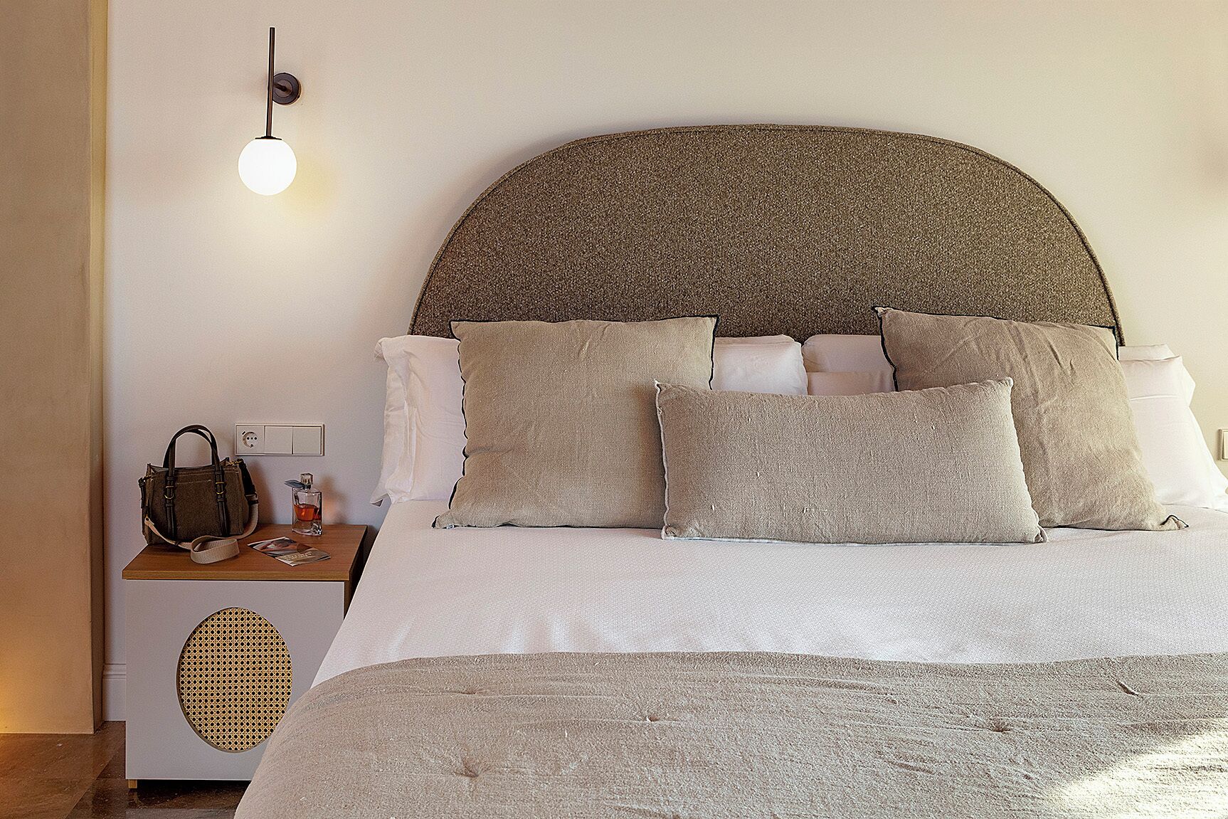 A neatly made bed with a large, textured headboard, a bedside table with a lamp, and a small speaker.