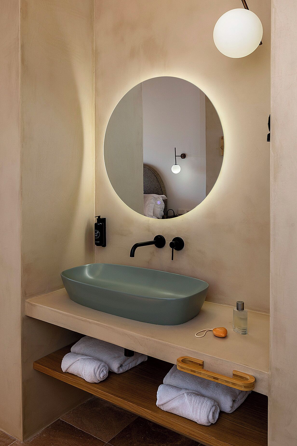 A bathroom with a round mirror, a beige sink, and a towel rack.