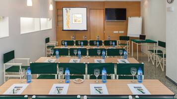 Un salón de conferencias con varias mesas, sillas, botellas de agua y una pantalla de presentación.