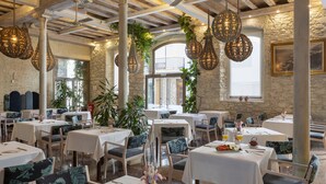 Un restaurant avec des tables et des chaises blanches, des luminaires suspendus et des murs en pierre.