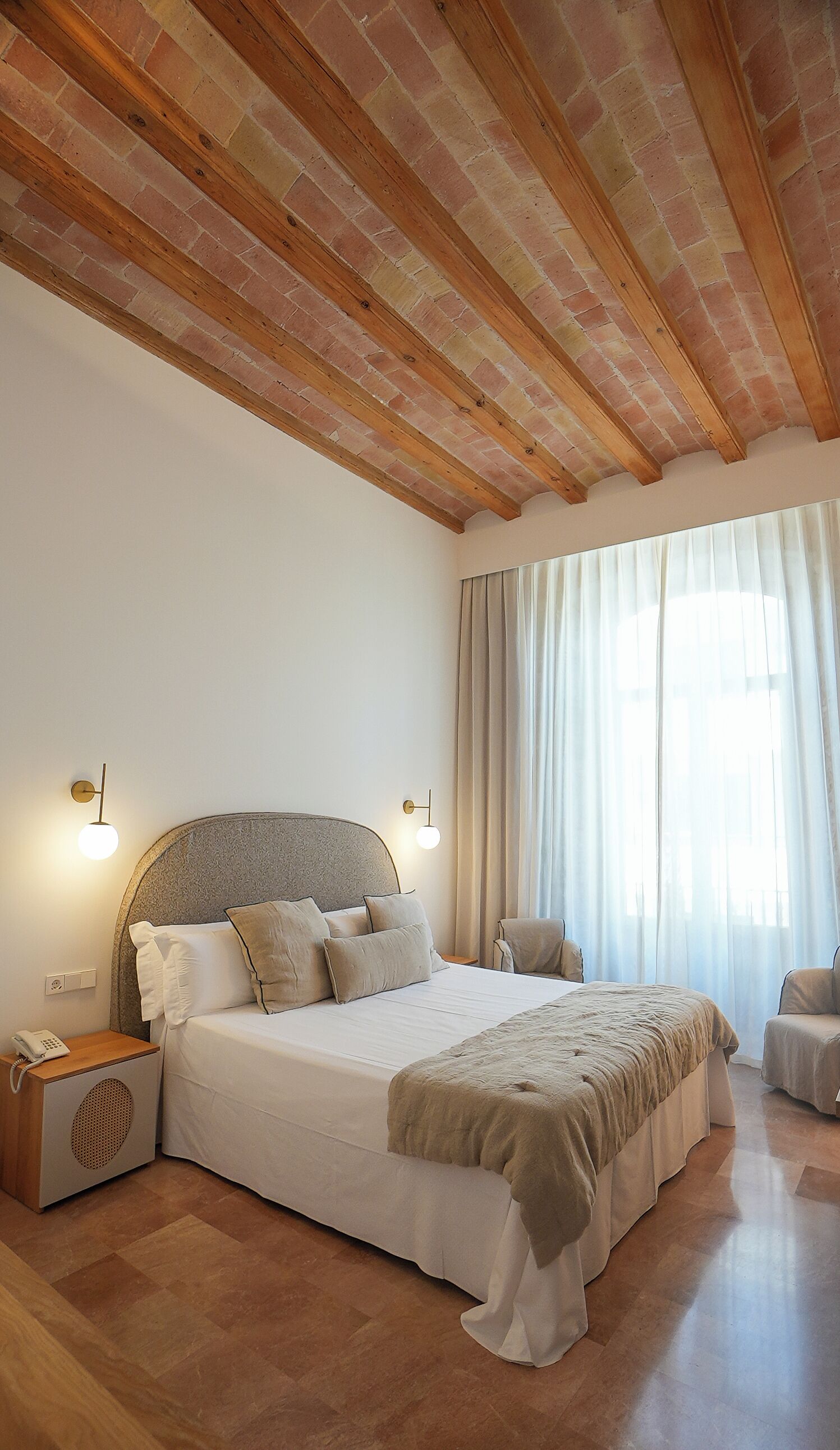 Un dormitorio con una cama grande, vigas de madera en el techo, una mesita de noche con un teléfono y una silla.