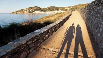 A coastal road with stone walls, a clear sky, and a distant view of houses and hills.