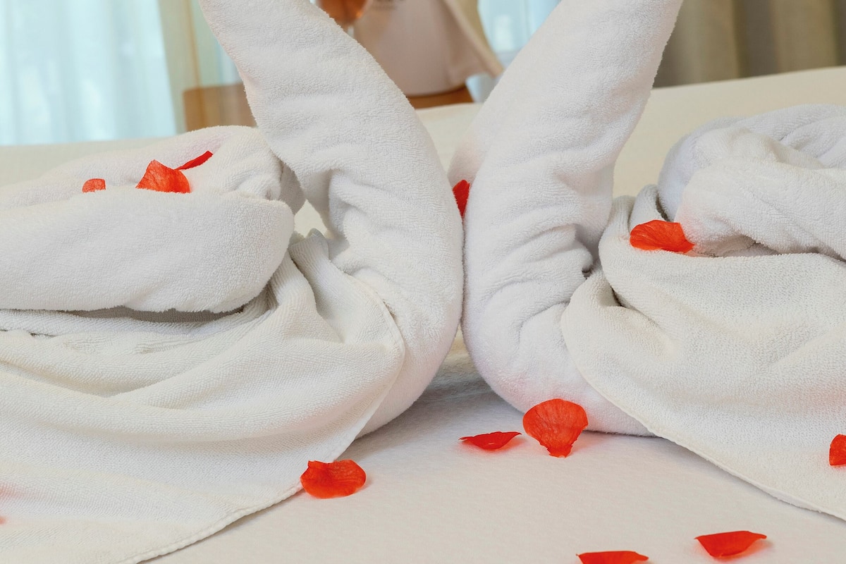 Une disposition de serviettes en forme de cœur, parsemée de pétales de rose.