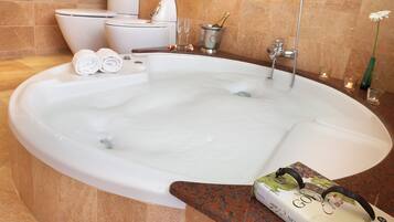 A large bathtub with a bottle of champagne, two rolled towels, and a book on the edge.