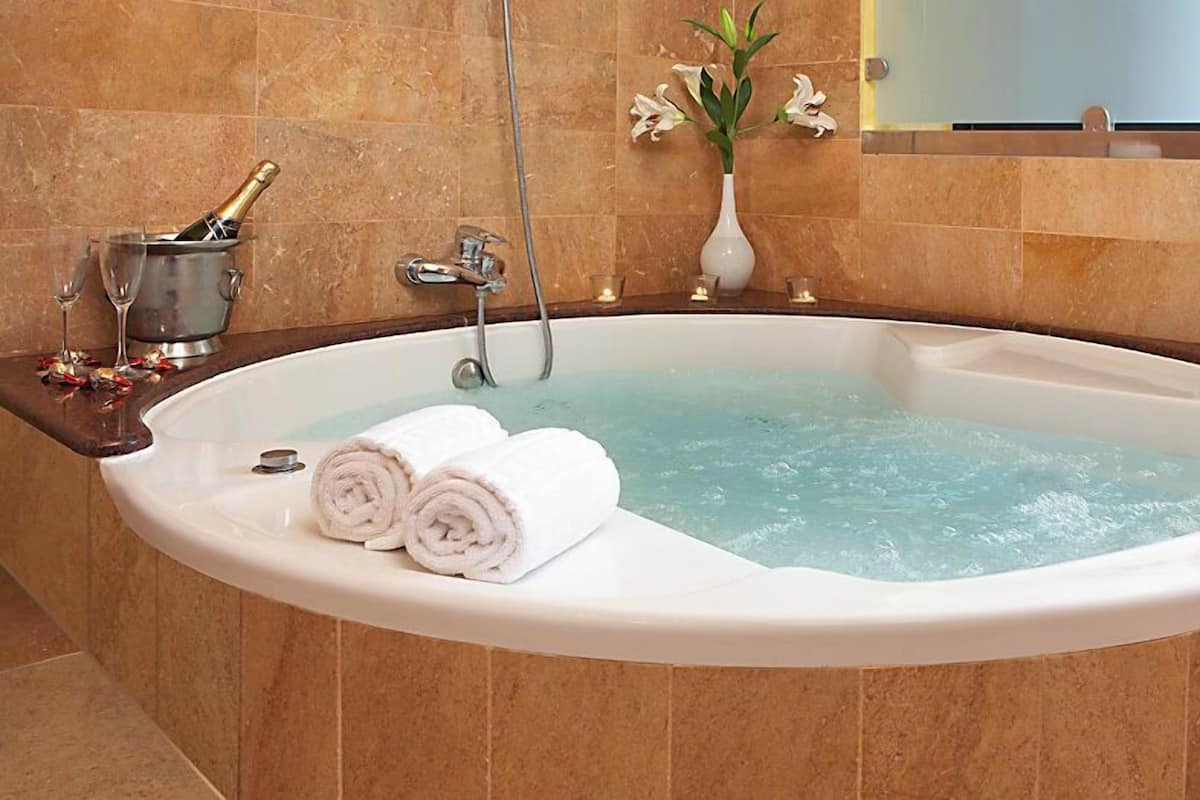 Une grande baignoire ovale, avec deux serviettes enroulées, une bouteille de champagne et un vase rempli de fleurs.