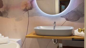 A modern bathroom with a white bathtub, a round mirror with a light halo, and a wooden vanity with a sink.