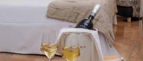 A hotel room with a neatly made bed, a bedside table with a bottle of champagne, glasses, and apples.