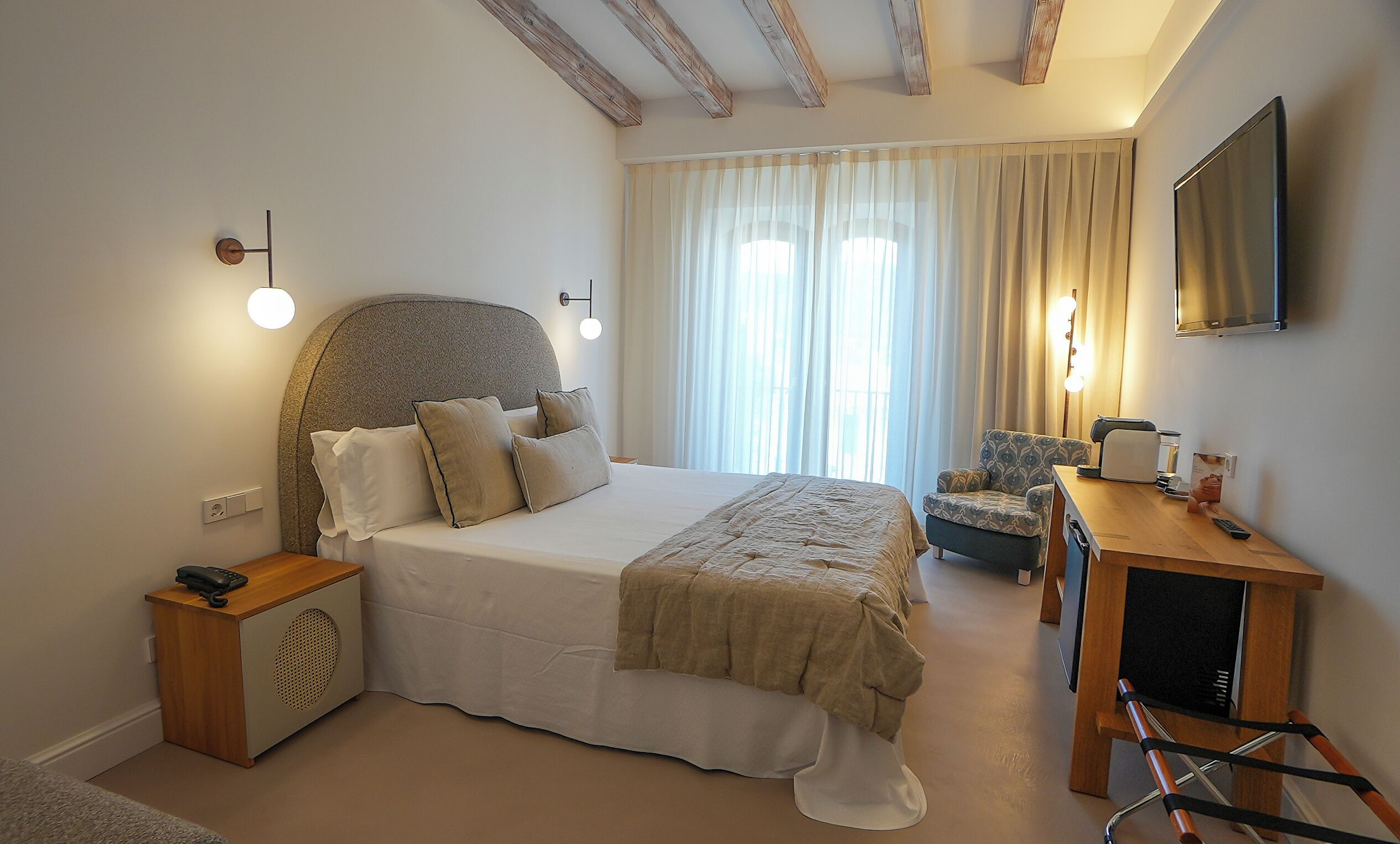 Un dormitorio con una cama grande, mesita de noche, silla, escritorio y televisor.