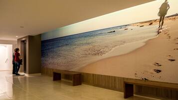 Un couloir orné d’une grande fresque représentant une scène de plage, avec un banc et une porte.