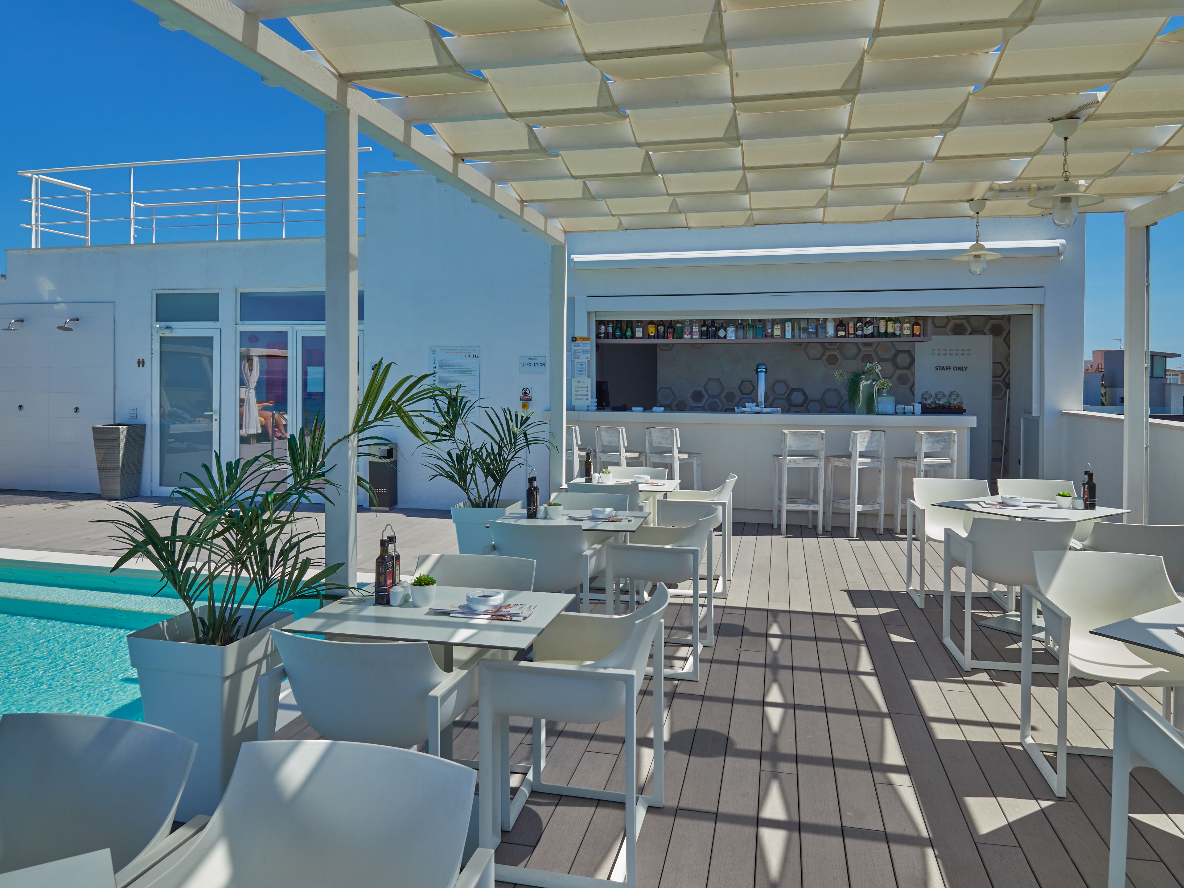 A rooftop bar with white furniture, a pool, and a bar area with a menu.