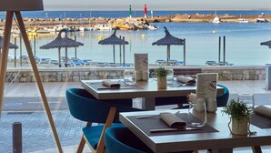 A seaside restaurant with tables and chairs, a menu, and a view of the sea and boats.
