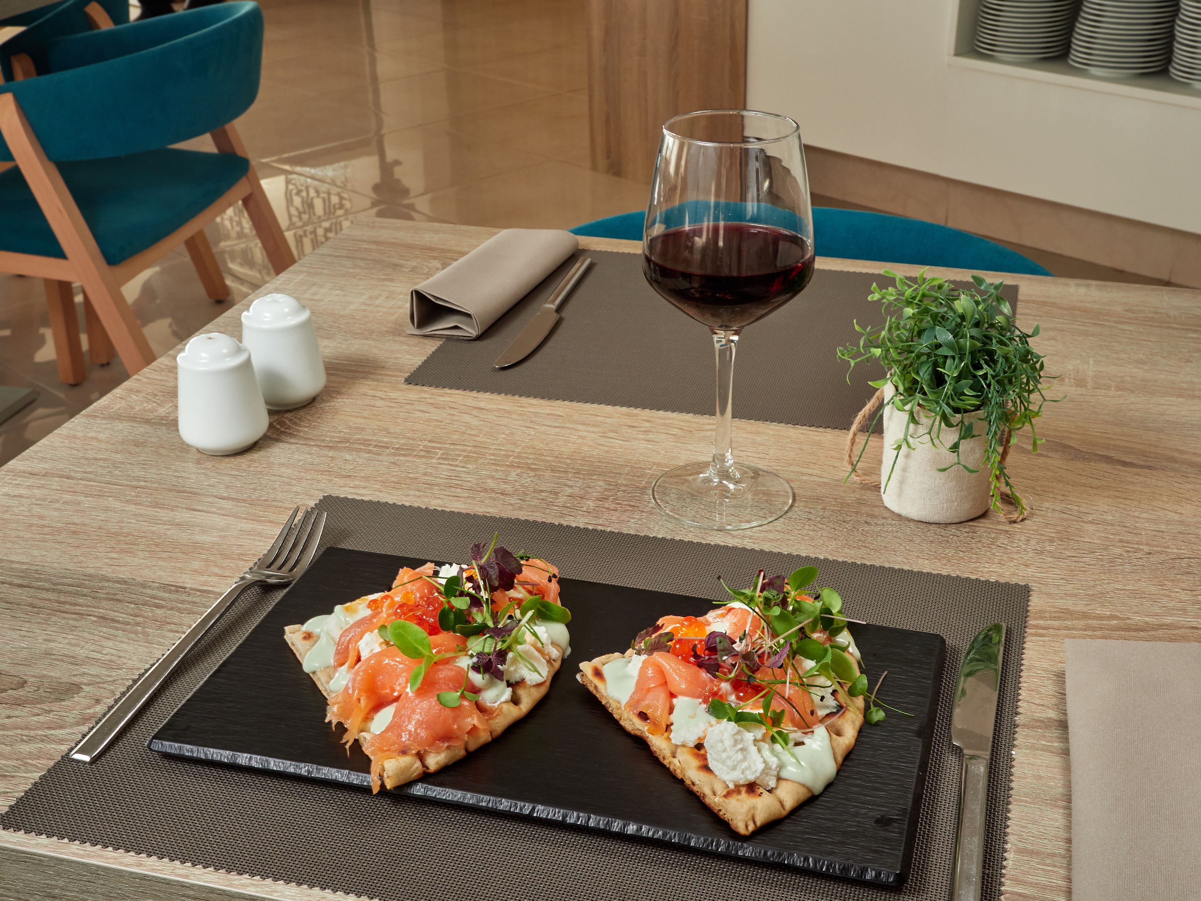 Una mesa de comedor con dos pizzas cubiertas de diversos ingredientes, una copa de vino tinto y una pequeña planta en maceta.