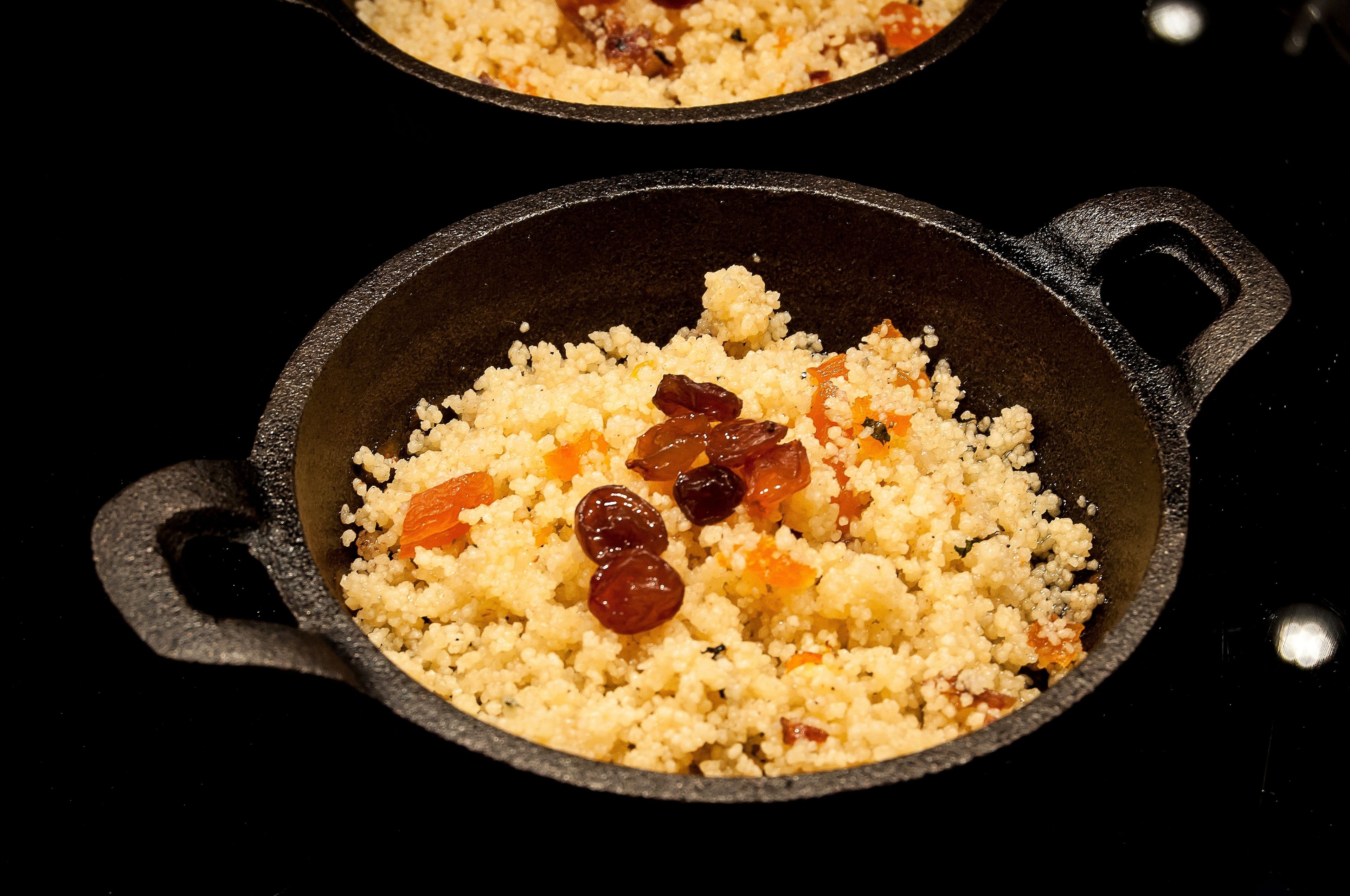 Deux poêlées en fonte contenant du couscous et des raisins secs.